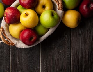 Colorful ripe apple fruits in basket on wooden table. Top view flat lay with copy space